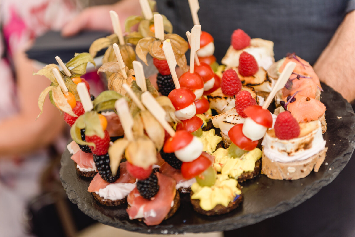 christian-lorenz.net Eine Platte mit verschiedenen Vorspeisen, darunter aufgespießtes Obst, Fleisch, Käse und Gemüse auf einem dunklen Servierteller.