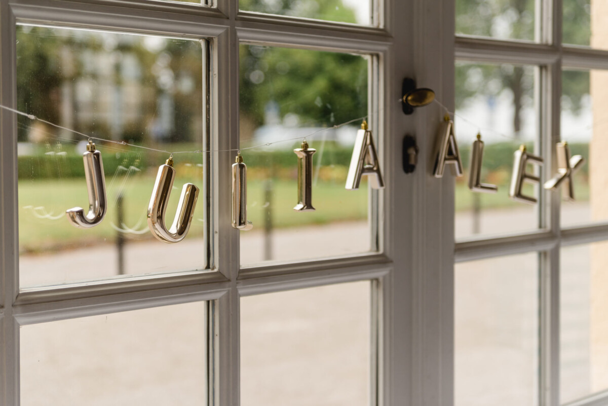 christian-lorenz.net Silberne Ballonbuchstaben mit der Aufschrift „JULIA ALEX“ sind über einem Fenster mit Blick ins Grüne aufgereiht.