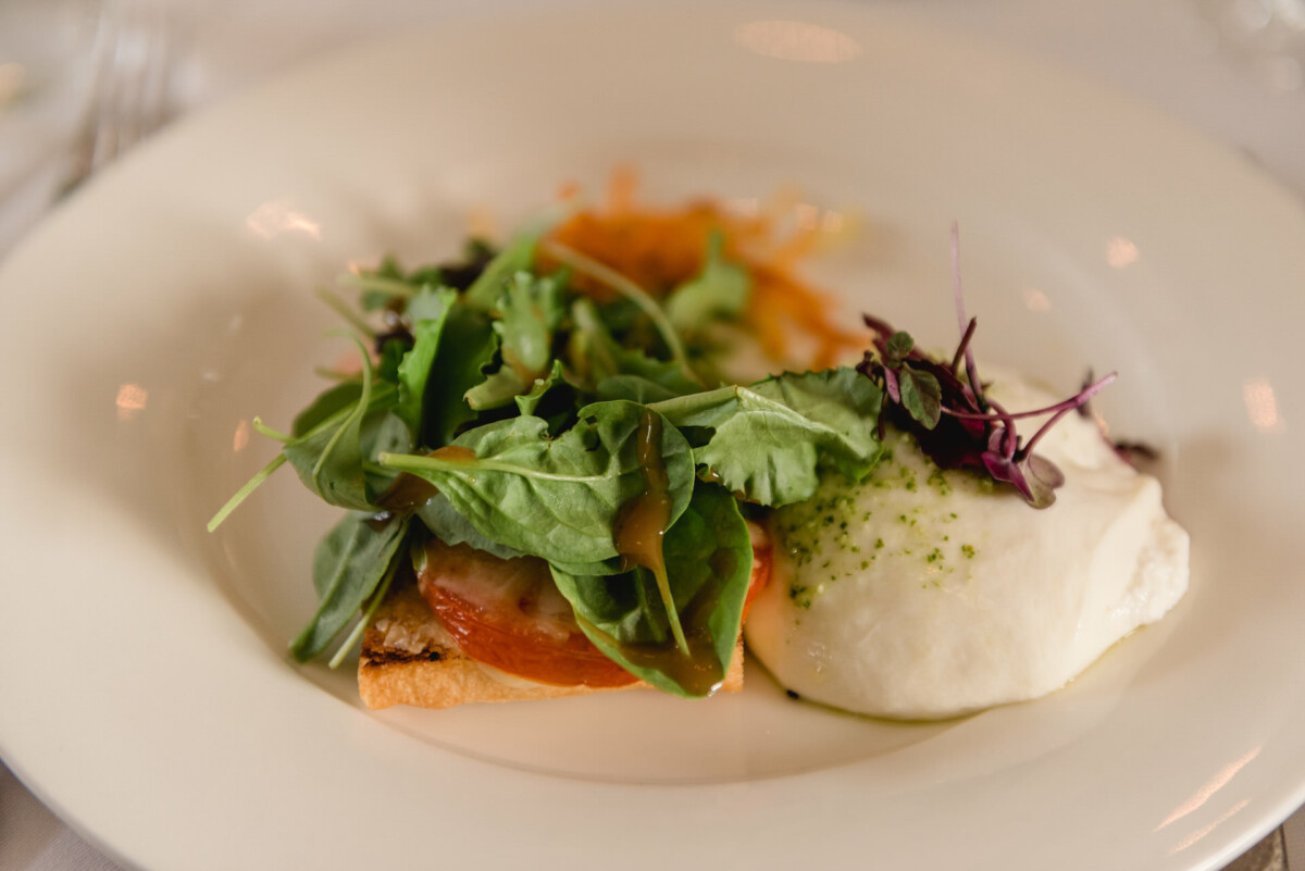 christian-lorenz.net Ein Teller Salat mit gemischtem Blattgemüse, einer Scheibe Tomate und einer Portion Weißkäse oder Burrata auf einem weißen Teller.