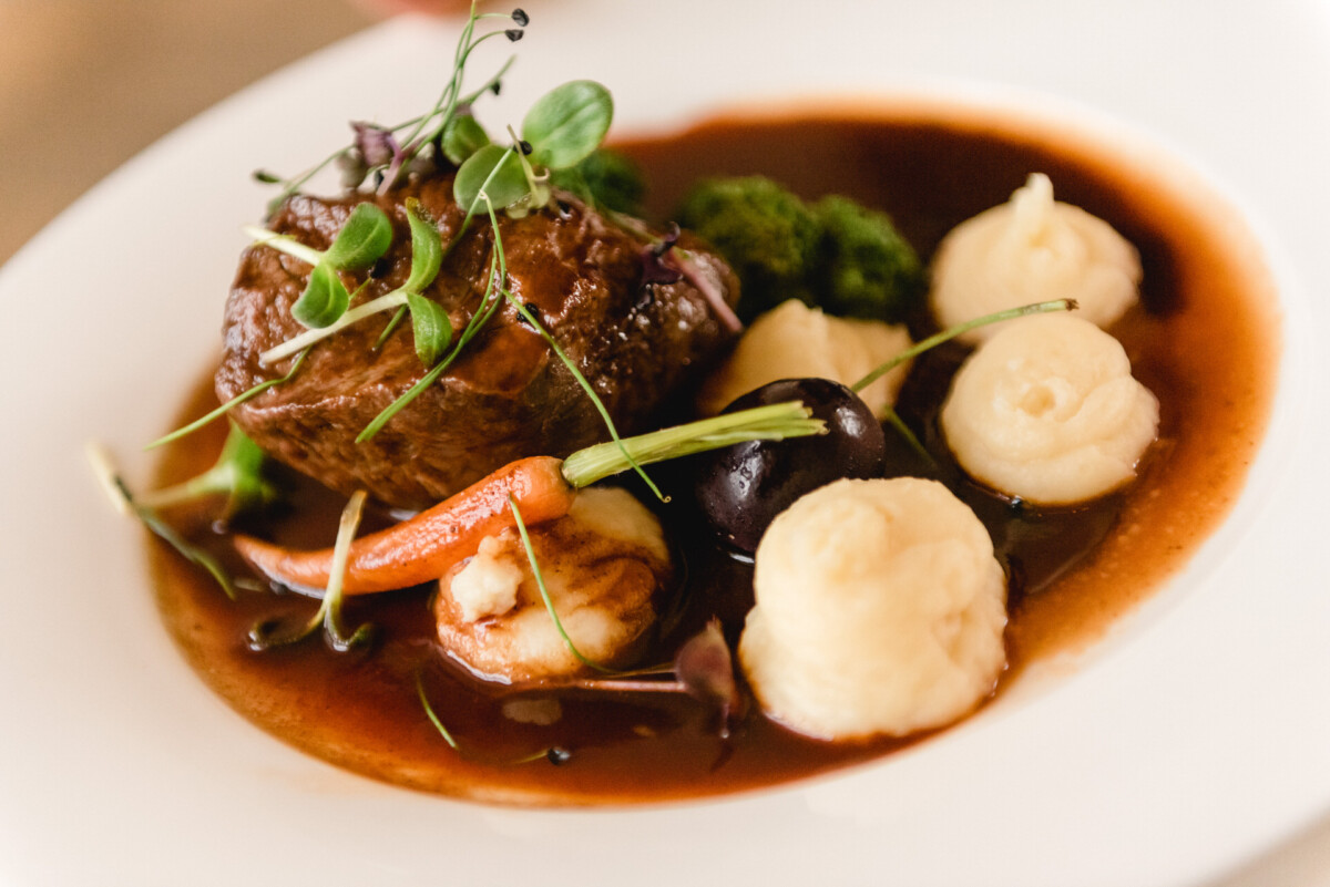 christian-lorenz.net Ein Tellergericht mit Rindfleisch mit Microgreens, mehreren Klecksen Kartoffelpüree, einer kleinen Karotte, Brokkoli und einer dunklen Soße.