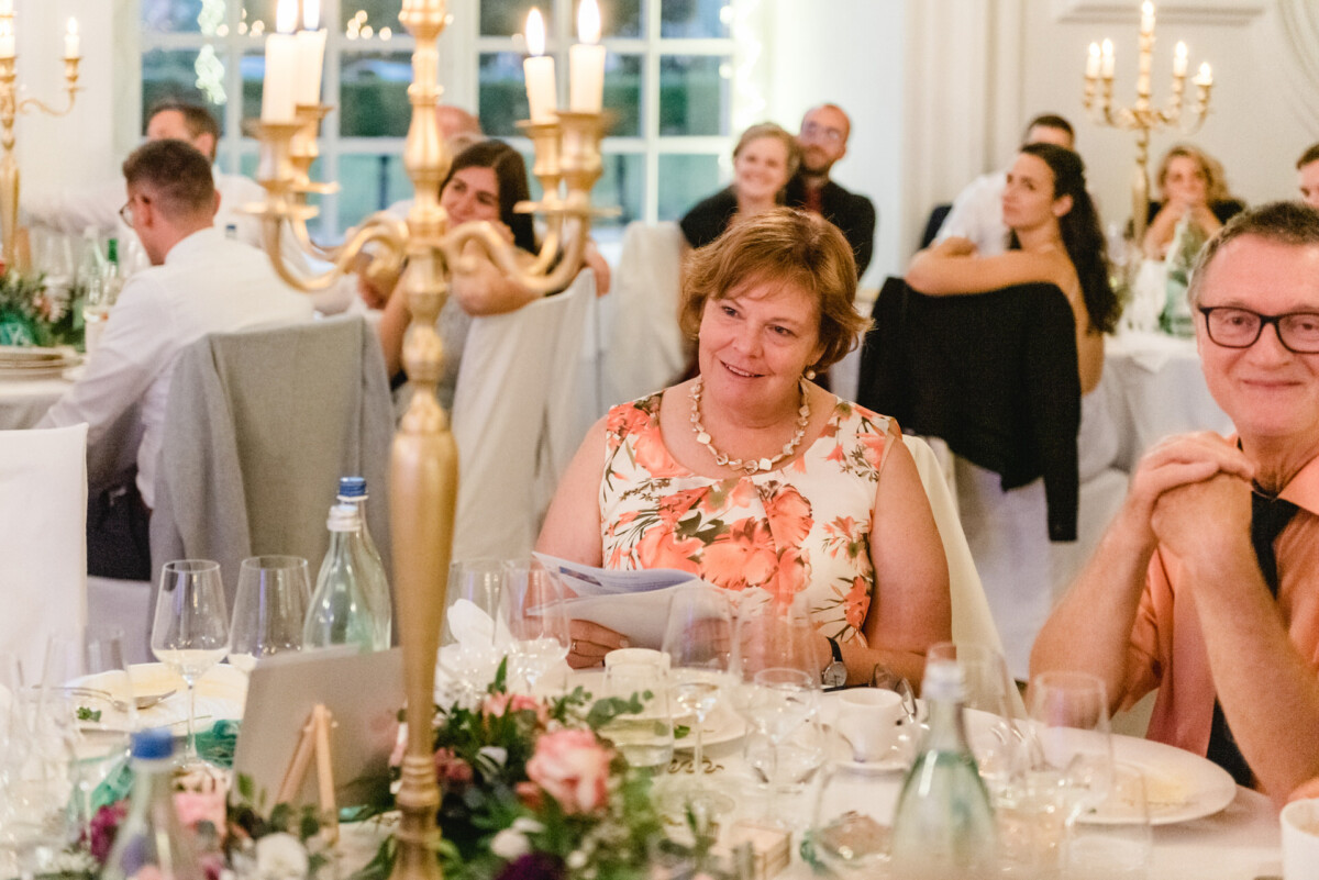 christian-lorenz.net Gäste sitzen an elegant gedeckten Tischen mit Blumenarrangements und Kandelabern und genießen eine Veranstaltung in einem gut beleuchteten Raum.