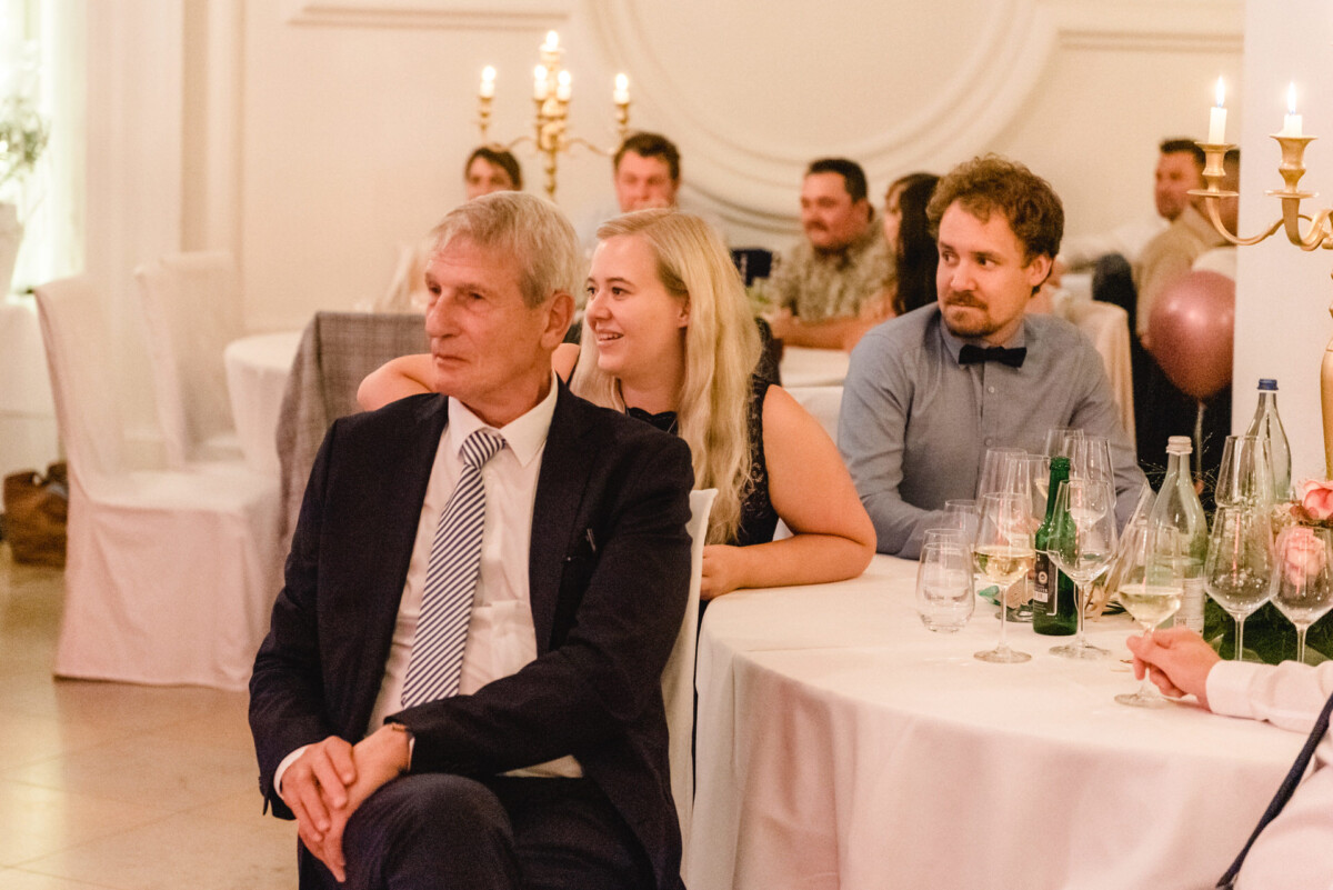 christian-lorenz.net An einem runden Tisch sitzen Menschen in formeller Kleidung. Sie scheinen einem Redner zuzuhören. Kerzen und Gläser schmücken den Tisch.