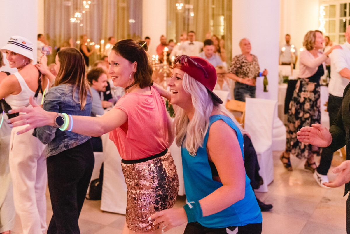 christian-lorenz.net Menschen tanzen bei einer Indoor-Veranstaltung, einige tragen legere und sportliche Kleidung. Im Hintergrund sind Tische und Gäste zu sehen.
