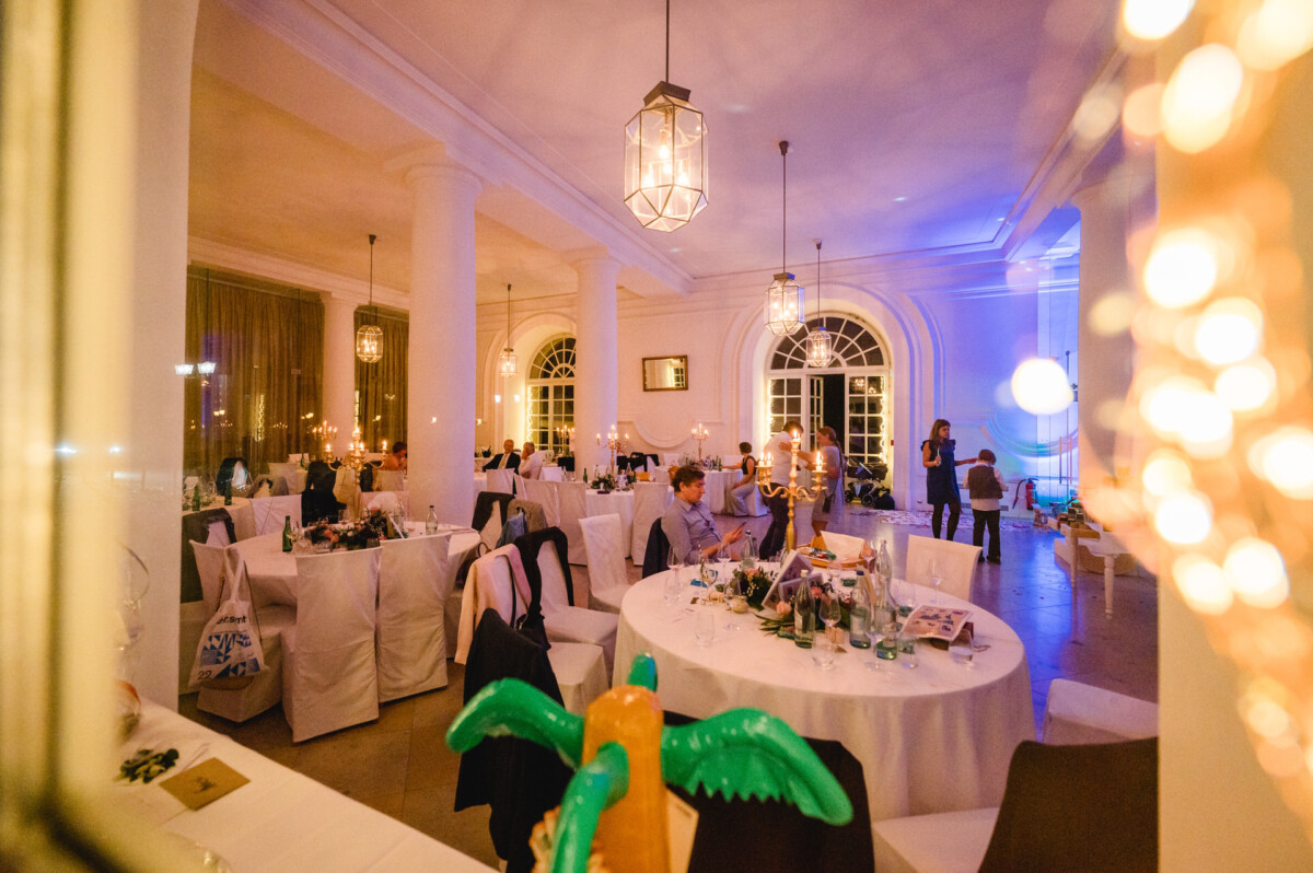christian-lorenz.net Ein hell erleuchteter, eleganter Speisesaal mit mehreren runden, weiß gedeckten Tischen. Wenige Gäste sitzen, im Vordergrund eine leuchtende, aufblasbare Dekoration.