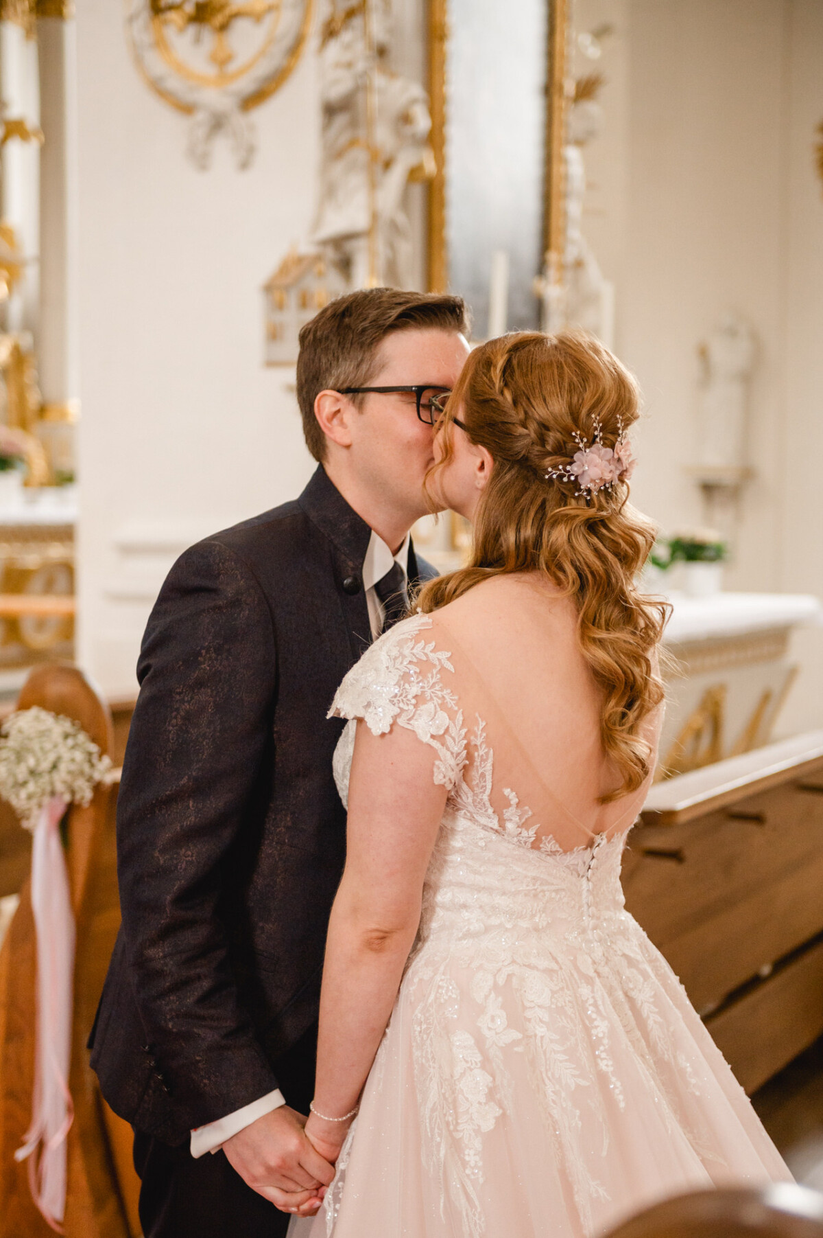 Ein Paar in Abendgarderobe küsst sich bei einer Hochzeitszeremonie in einem dekorierten Veranstaltungsort.