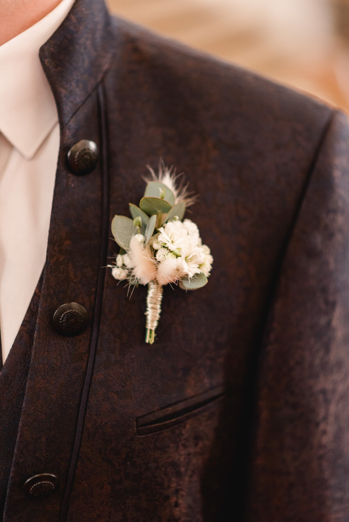 christian-lorenz.net Eine Person in einer dunklen, strukturierten Jacke mit einem weißen Hemd darunter trägt eine Ansteckblume aus weißen Blumen und grünen Blättern am Revers.
