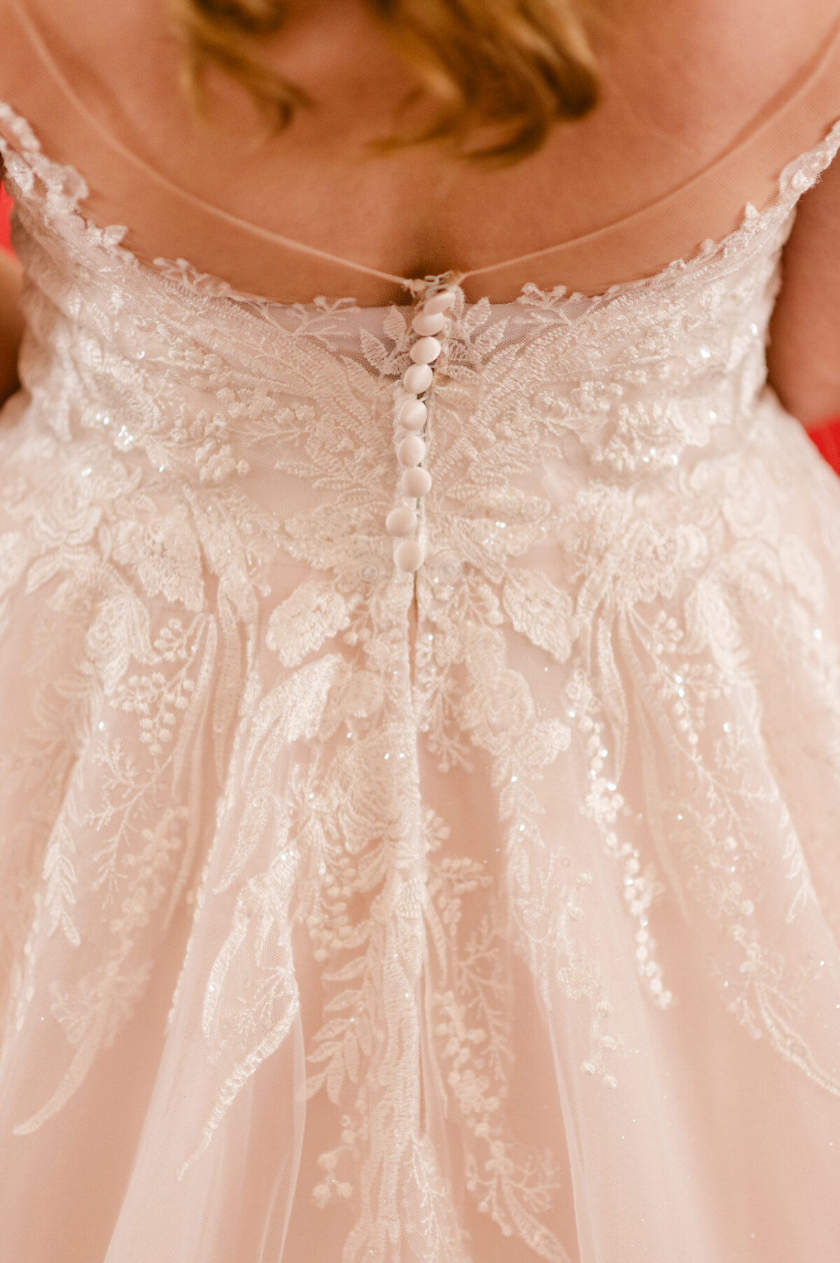 christian-lorenz.net Nahaufnahme der Rückseite des Spitzenbrautkleides einer Braut. Auf der Rückseite sind komplizierte Blumenmuster und eine Reihe kleiner weißer Knöpfe zu sehen.