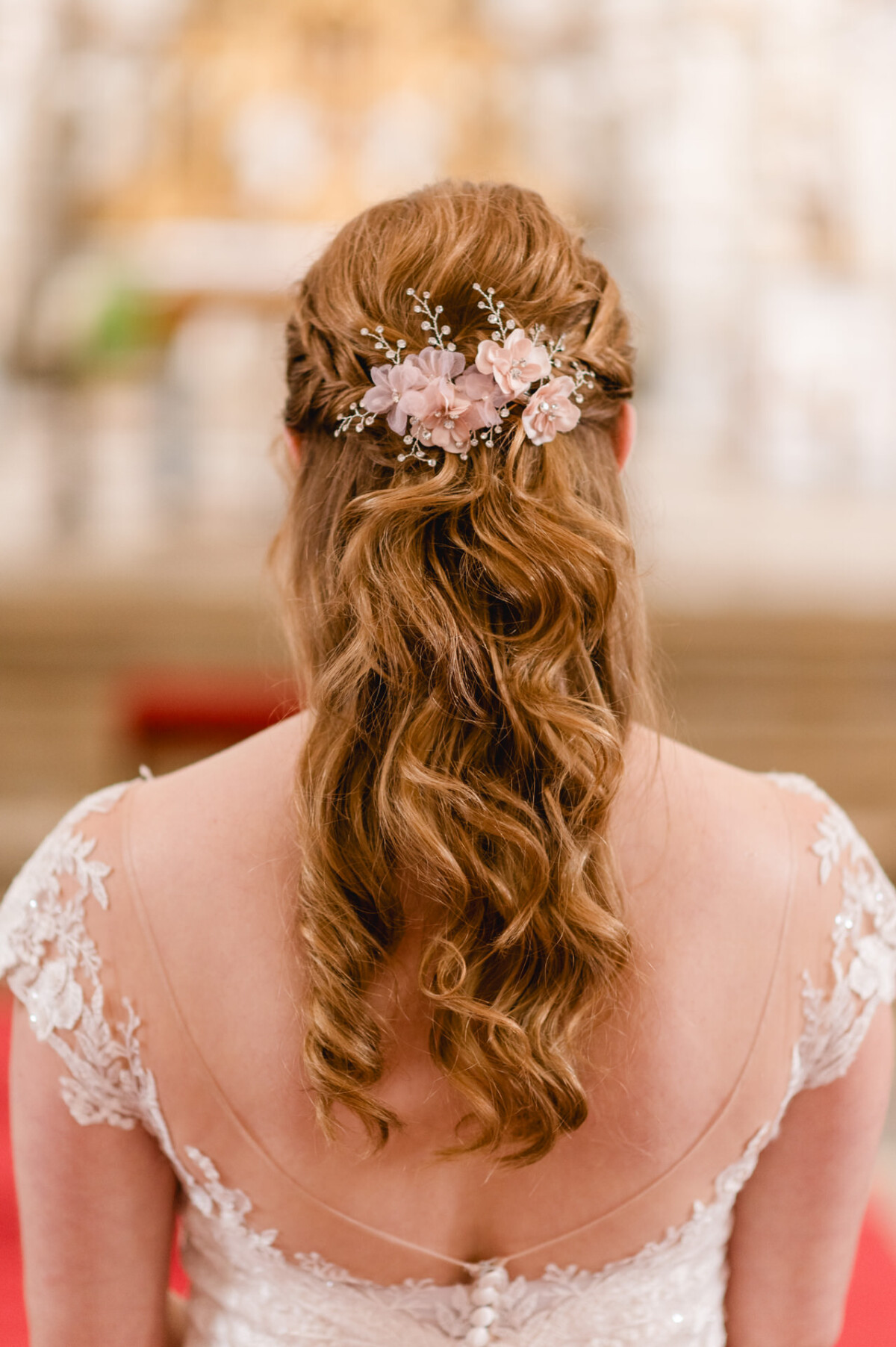 christian-lorenz.net Rückansicht einer Braut mit welligem Haar, gestylt mit floralen Accessoires, in einem weißen Spitzenkleid.