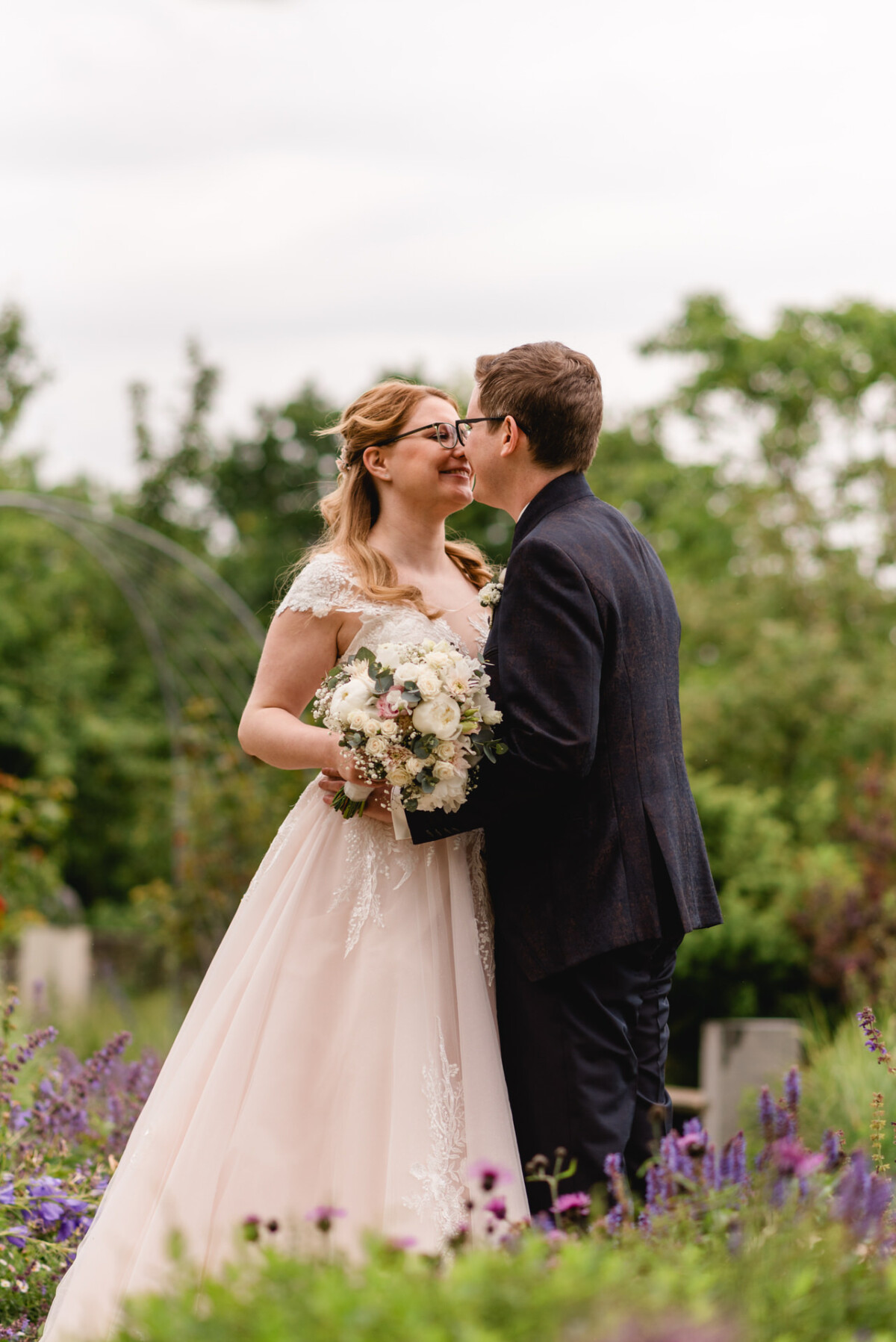 christian-lorenz.net Braut und Bräutigam stehen eng beieinander in einem Garten; die Braut hält einen Strauß weißer Blumen.