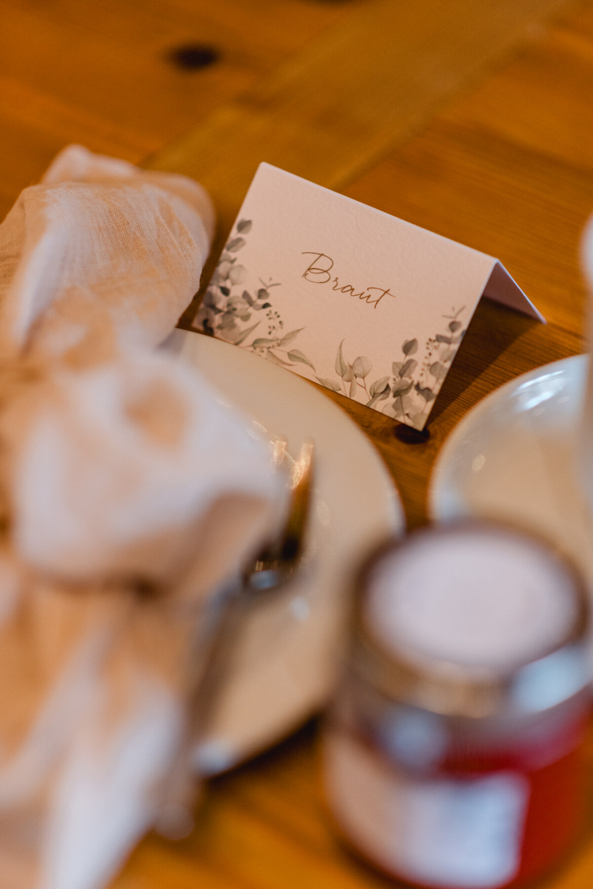 christian-lorenz.net Ein gedeckter Tisch mit einer gefalteten Karte mit der Aufschrift „Briat“, einer beigen Serviette, einem weißen Teller und einem unscharfen Glas im Vordergrund auf einem Holztisch.