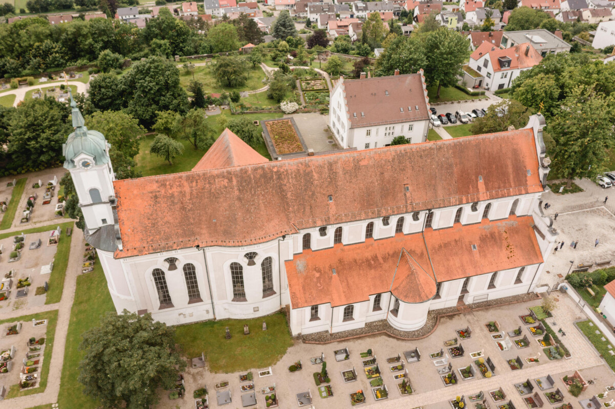 Luftaufnahme eines großen Gebäudes mit rotem Ziegeldach, umgeben von einem Friedhof und Grünflächen.