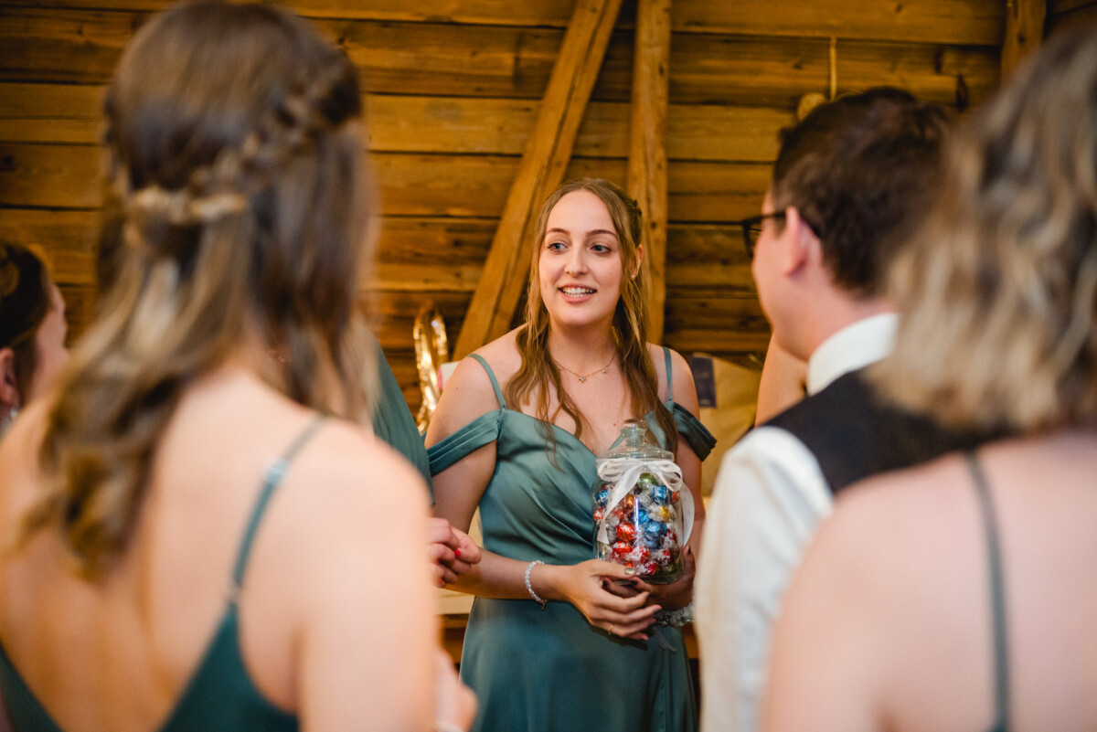 2024.10.05-Lea-Viktor-Hochzeit-Schammenhof-Langenau-bei-Ulm-01011 Bei einer Hochzeit im Schammenhof in Langenau bei Ulm hält eine Frau in einem grünen Kleid eine durchsichtige Tüte mit bunten Süßigkeiten in der Hand und mischt sich in dem charmanten Holzlokal unter die in Abendgarderobe gekleideten Gäste.