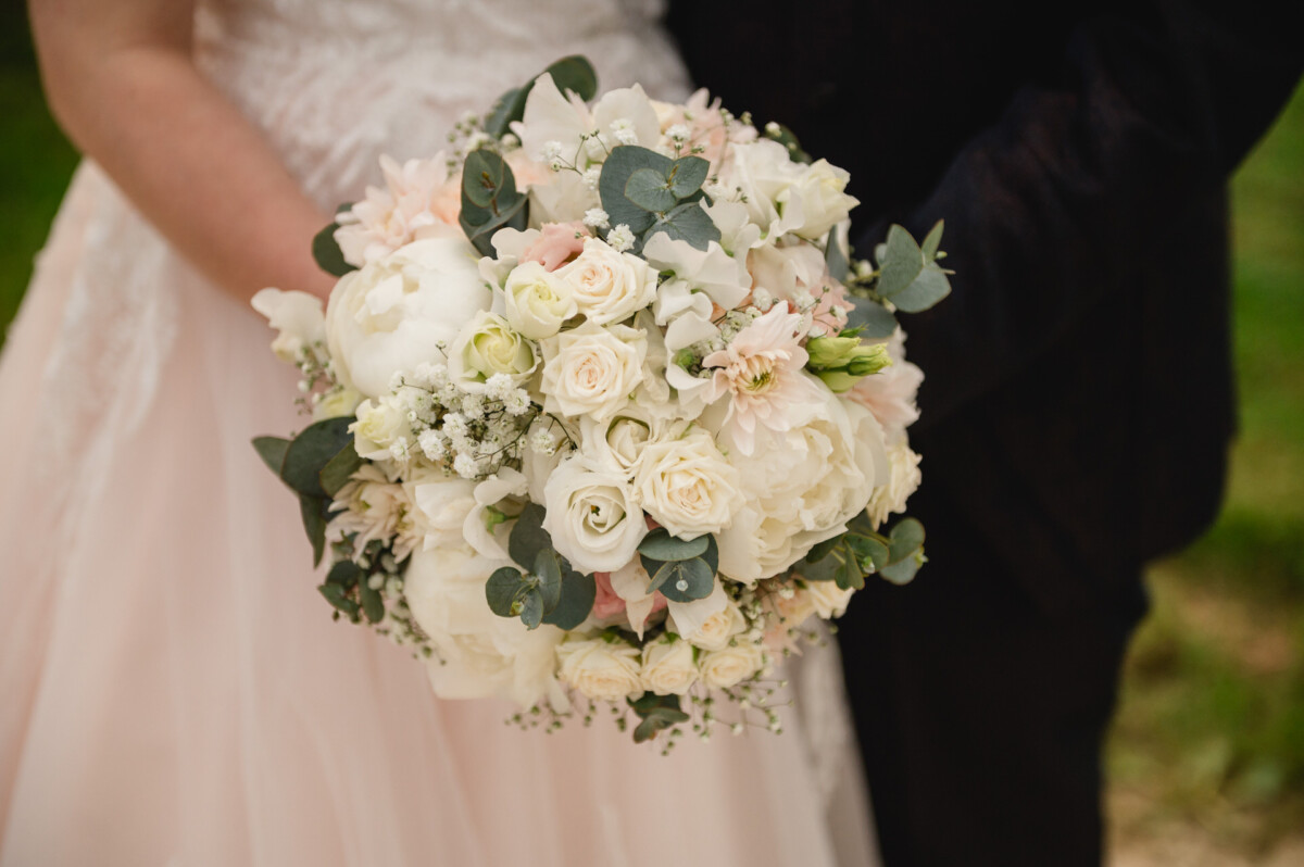2024.10.05-Lea-Viktor-Hochzeit-Schammenhof-Langenau-bei-Ulm-01147 Auf dem Hochzeits-Schammenhof in Langenau bei Ulm steht eine Braut in ihrem hellrosa Kleid anmutig neben einer dunkel gekleideten Braut und hält einen Strauß weißer und rosa Blumen mit Grün in der Hand.
