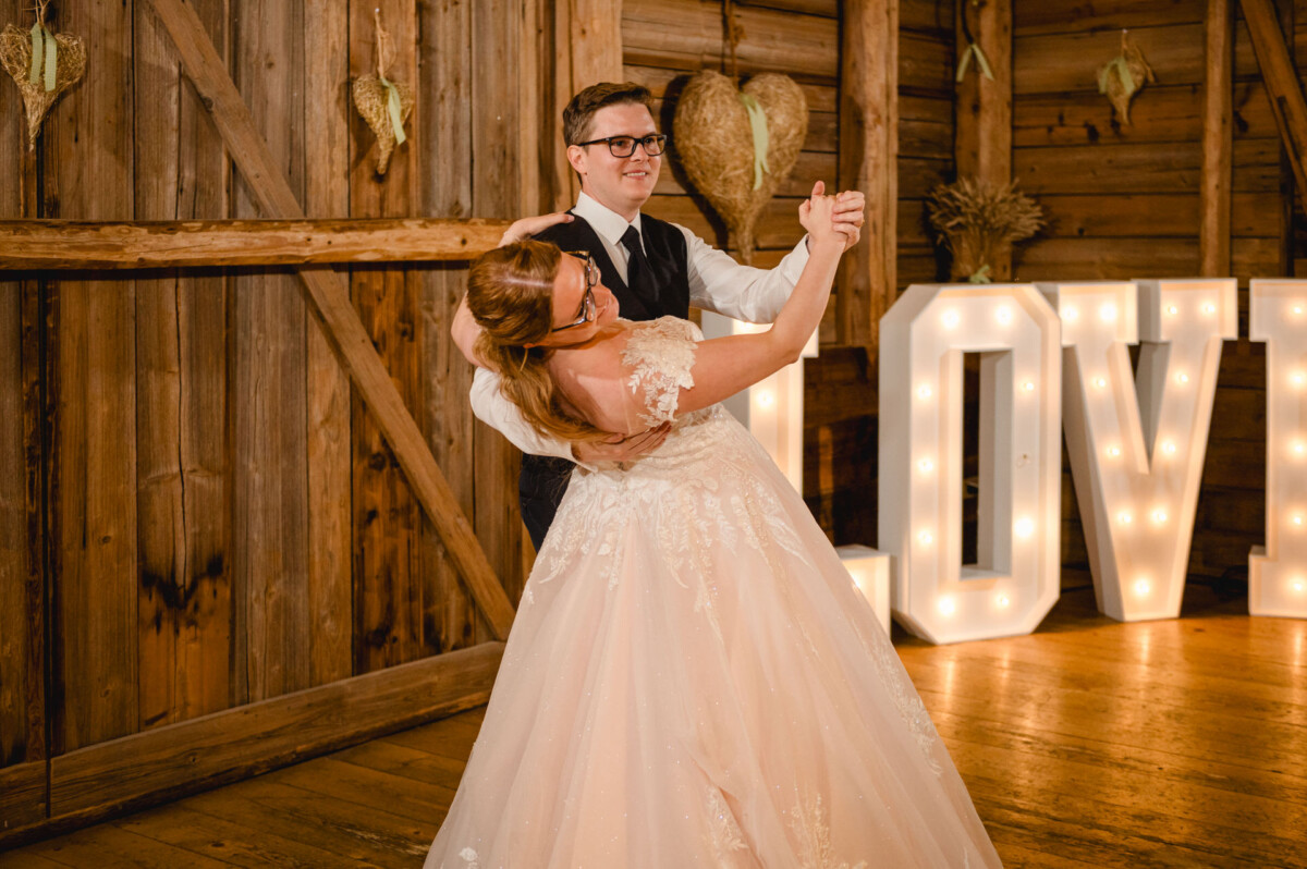 Bei der Hochzeit im Schammenhof, Langenau bei Ulm, tanzt ein Paar anmutig in einem rustikalen Veranstaltungsort mit Holzwänden und großen Leuchtbuchstaben mit der Aufschrift „LOVE“, die eine bezaubernde Kulisse schaffen. Bei der Hochzeit im Schammenhof, Langenau bei Ulm, tanzt ein Paar anmutig in einem rustikalen Veranstaltungsort mit Holzwänden und großen Leuchtbuchstaben mit der Aufschrift „LOVE“, die eine bezaubernde Kulisse schaffen.