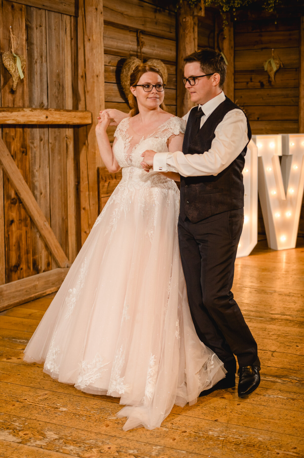 Auf dem Hochzeit Schammenhof bei Langenau Ulm tanzt ein Paar gemeinsam auf einem Holzboden in rustikalem Ambiente, die Frau im weißen Brautkleid und der Mann mit Weste und Krawatte. Auf dem Hochzeit Schammenhof bei Langenau Ulm tanzt ein Paar gemeinsam auf einem Holzboden in rustikalem Ambiente, die Frau im weißen Brautkleid und der Mann mit Weste und Krawatte.