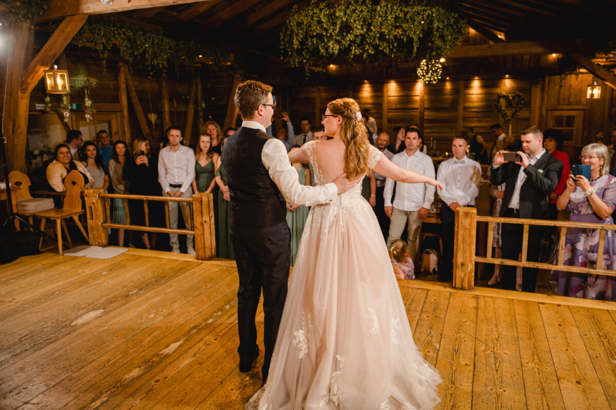 Anmutig tanzen Braut und Bräutigam auf dem Holzboden der charmanten Hochzeit im Schammenhof in Langenau. Die Gäste, fasziniert von diesem Moment, stehen und sitzen rund um den rustikalen Veranstaltungsort bei Ulm und schießen Fotos, um die fröhliche Feier festzuhalten. Anmutig tanzen Braut und Bräutigam auf dem Holzboden der charmanten Hochzeit im Schammenhof in Langenau. Die Gäste, fasziniert von diesem Moment, stehen und sitzen rund um den rustikalen Veranstaltungsort bei Ulm und schießen Fotos, um die fröhliche Feier festzuhalten.