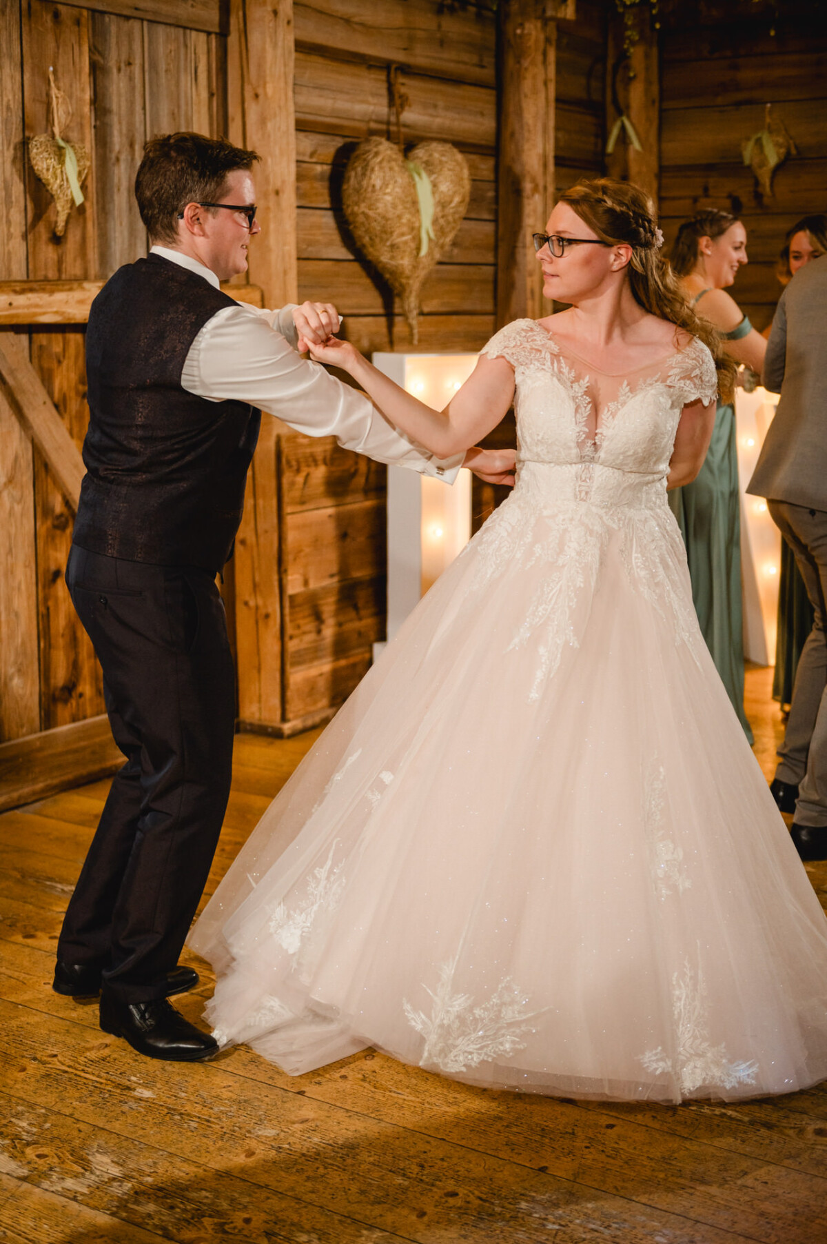 Bei der Hochzeit im Schammenhof, in der Nähe von Langenau und Ulm, tanzen eine Braut im weißen Kleid und ein Bräutigam in einer Weste anmutig in einem rustikalen Holzsaal, der mit einer großen Herzdekoration geschmückt ist. Bei der Hochzeit im Schammenhof, in der Nähe von Langenau und Ulm, tanzen eine Braut im weißen Kleid und ein Bräutigam in einer Weste anmutig in einem rustikalen Holzsaal, der mit einer großen Herzdekoration geschmückt ist.