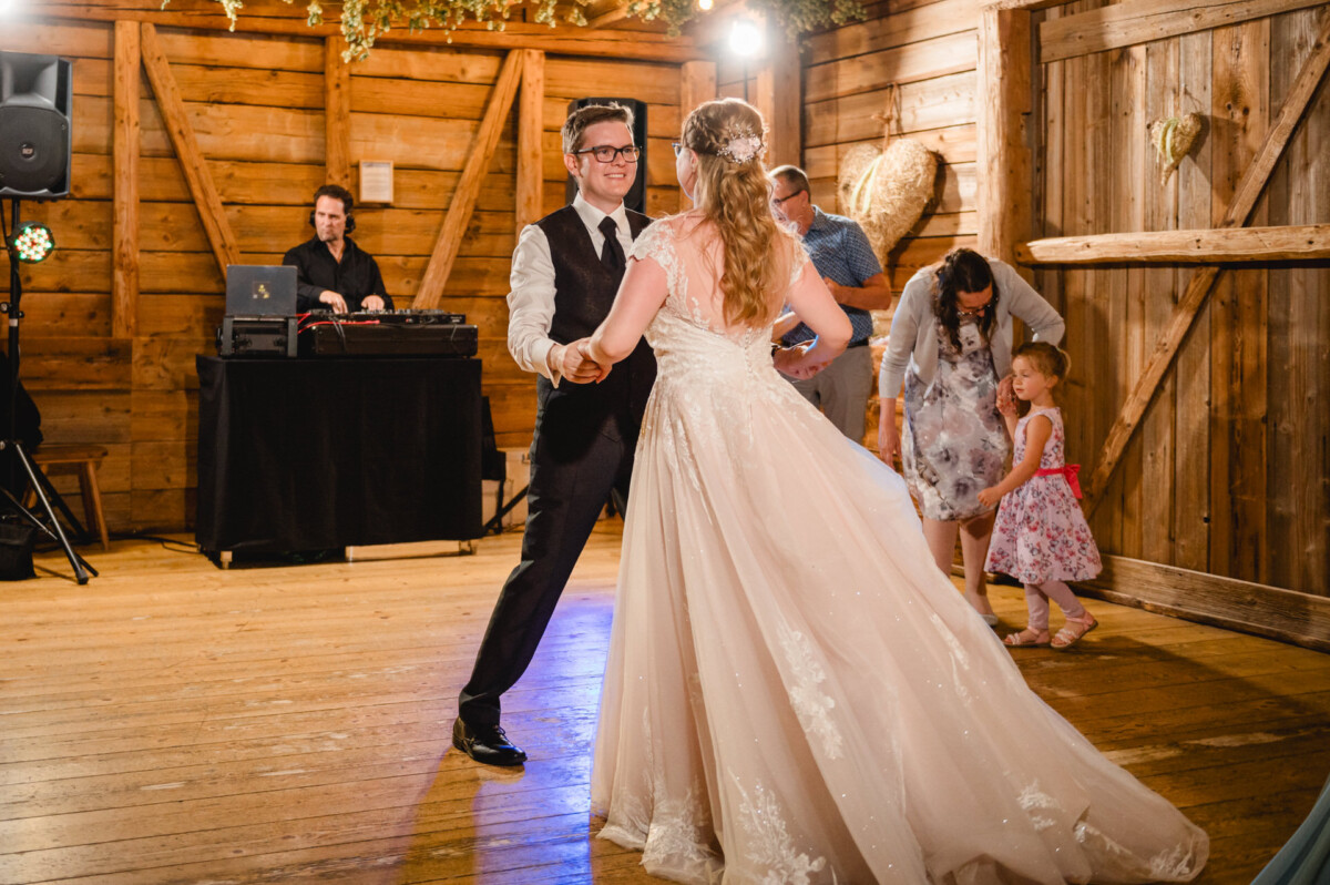 Bei der Hochzeit im Schammenhof in Langenau bei Ulm tanzen Braut und Bräutigam gemeinsam in einer rustikalen Holzhalle, im Hintergrund spielt ein DJ. Ein Paar schaut zu, während ein kleines Mädchen sein rosa Plüschtier umklammert. Bei der Hochzeit im Schammenhof in Langenau bei Ulm tanzen Braut und Bräutigam gemeinsam in einer rustikalen Holzhalle, im Hintergrund spielt ein DJ. Ein Paar schaut zu, während ein kleines Mädchen sein rosa Plüschtier umklammert.